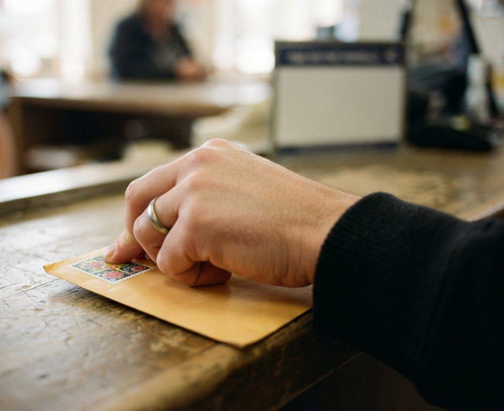 A postal clerk sorts stamped letters on a counter inside a post office.